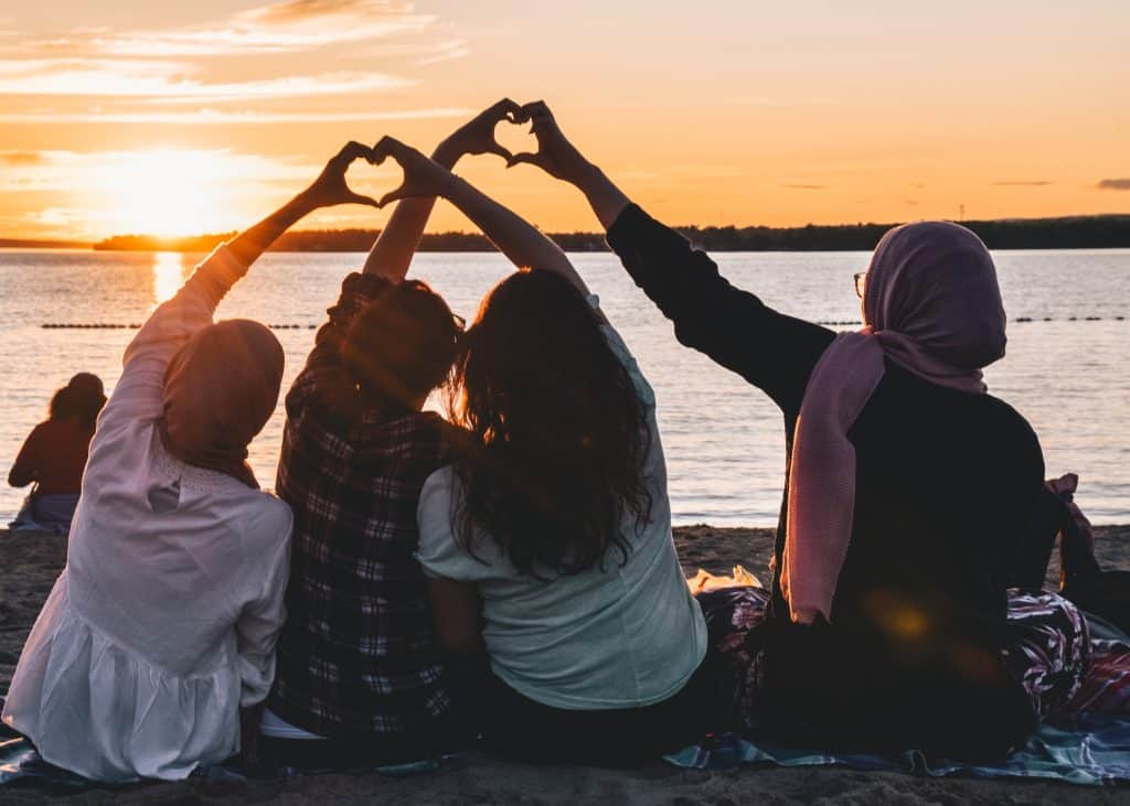 Four friends putting their fingers together to make hearts in the sunset. Make time to connect with those you love. 